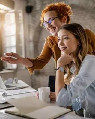 empresarias-felizes-lendo-um-e-mail-no-computador-enquanto-trabalham-juntas-no-escritorio-o-foco-esta-na-mulher-ruiva